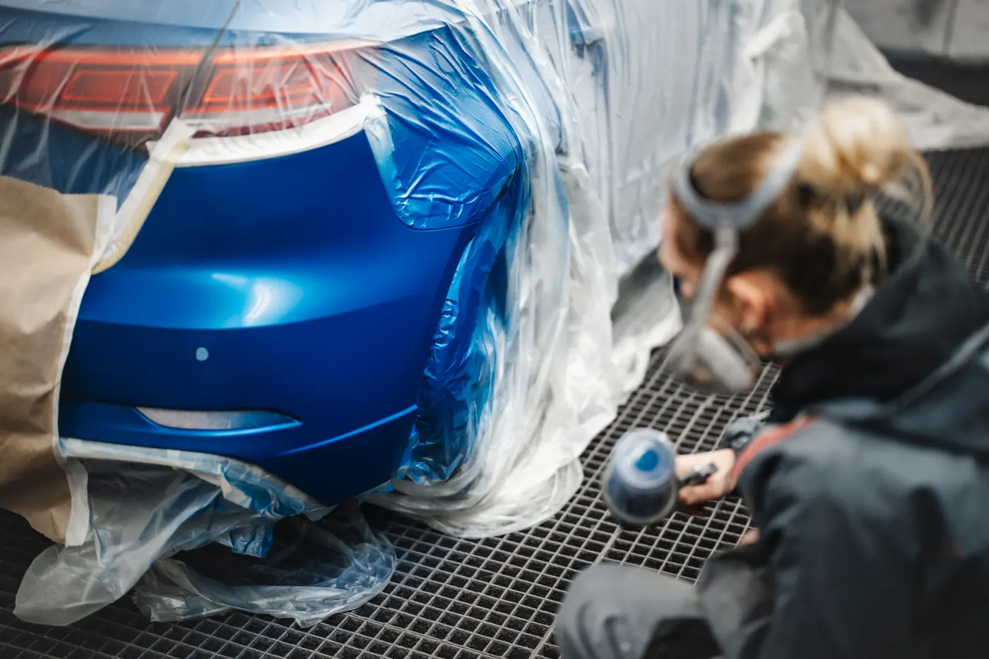 Lackiererin in der Lackierkabine an einem blauen Fahrzeug